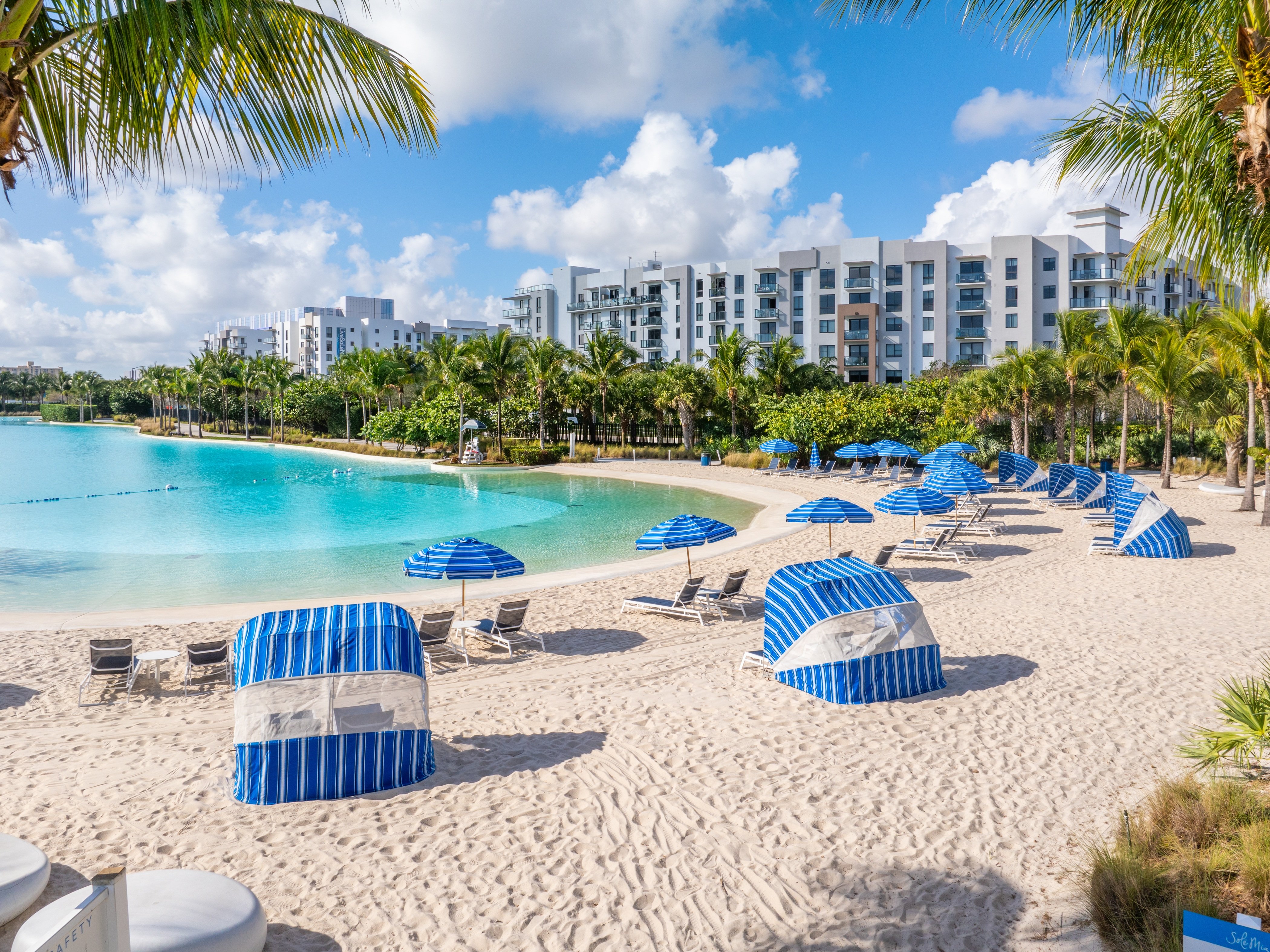 A beach scene with blue umbrellas and a pool.